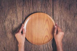 Top view hand holding plate on wood background.