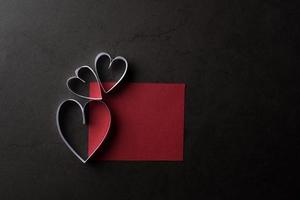 White heart shaped paper in shadow red note card on black background.