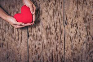 mano que sostiene el corazón rojo sobre fondo de madera. foto