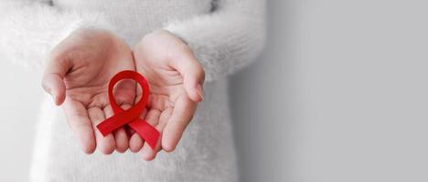 Red ribbon on woman hands for world aids day with copy space