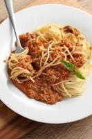 Close up a fork with spaghetti and red sauce on cutting board photo