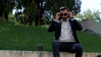 hombre con barba en un traje clásico se pone gafas de sol video