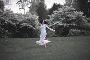 Mujer feliz en vestido blanco bailando en un parque de la ciudad en flor foto