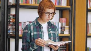 giovane donna con gli occhiali legge un libro in biblioteca video