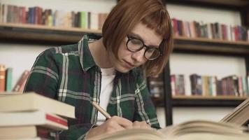 Una joven pelirroja lee un libro en una biblioteca.