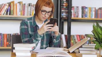 junge Frau schaut in der Bibliothek auf ihr Handy