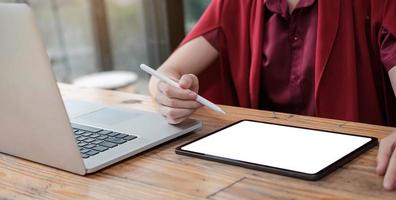 Woman using tablet screen blank and laptop on the table mock up photo