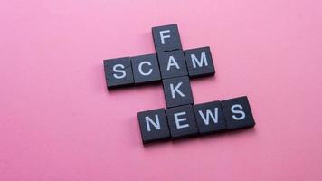 A group of scrabble tile forming word scam fake news. Selective focus on the tiles isolated on pink background photo