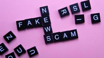 A group of scrabble tile forming word scam fake news. Selective focus on the tiles isolated on pink background photo