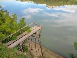 el puente alto de tablas de pino en la orilla del río para pescar foto