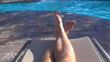 pov de las piernas de un hombre al borde de la piscina de un hotel resort.