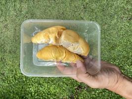 una mano sosteniendo durians dentro de un recipiente de plástico, listo para llevar. foto