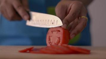 Chef mujer cortando tomate en tabla de cortar en la cocina.