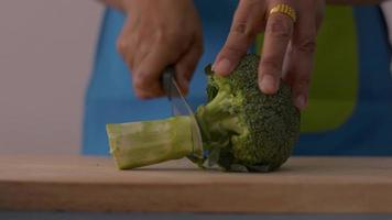 Woman cutting broccoli on wooden cutting board in the kitchen. video