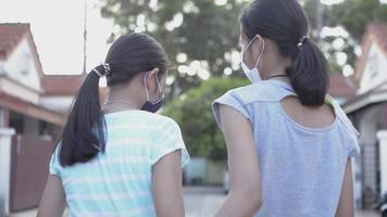 Vista trasera de dos hermanas usan mascarilla abrazándose en el camino. video