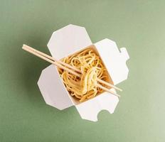 Caja de papel wok abierta con fideos y palillos. foto