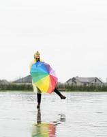 Beautiful brunette woman holding colorful umbrella dancing in the rain photo