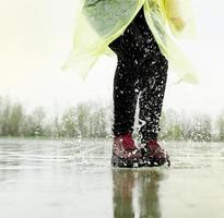 mujer jugando bajo la lluvia, saltando en charcos con salpicaduras foto