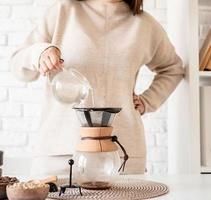 woman brewing coffee in coffee pot, pouring hot water into the filter photo