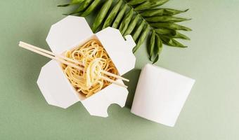 Caja de papel wok abierta con fideos y palillos. foto