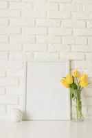 tulipanes amarillos en un jarrón de vidrio y marco de fotos en blanco