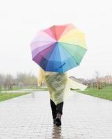 Mujer sosteniendo coloridos paraguas caminando bajo la lluvia, vista desde atrás foto