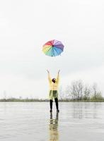 Brunette woman throwing colorful umbrella up in the rain photo