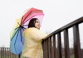 Mujer de pie afuera sosteniendo un paraguas de colores, mirando a otro lado foto