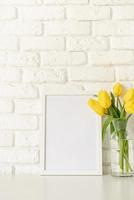 Yellow tulips in a glass vase and blank photo frame