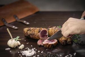 Cortar una porción de rosbif orgánico con un cuchillo en la mesa de madera con ajo, pimienta y sal en Melbourne, Australia