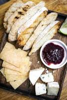 Rustic mixed cheese board platter with toasted bread and redcurrant jam on wooden tray photo