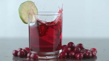 Ice splashing into cranberry juice in slow motion video