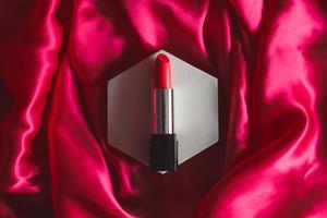 lápiz labial rojo sobre un fondo de seda con textura, cosméticos de belleza. foto