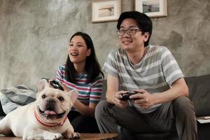 Asian couple is playing video games and pet dog nearby.