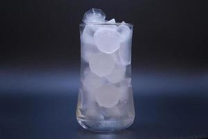 El hielo en un vaso de agua transparente se derrite sobre fondo negro.