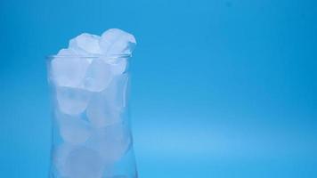 el hielo en un vaso de agua transparente derritiéndose sobre fondo azul. foto
