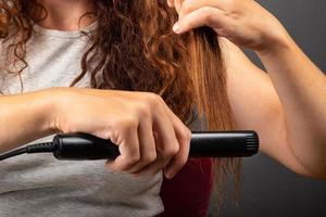 Girl smooths curly hair with a hair straightener, curling iron. photo