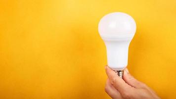 LED light bulb in hand with copy space on yellow background