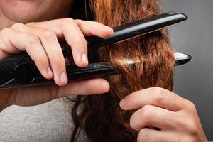 chica endereza el cabello rizado con una plancha. foto