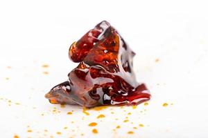 A piece of dark amber cannabis wax concentrate close up on white paper. photo