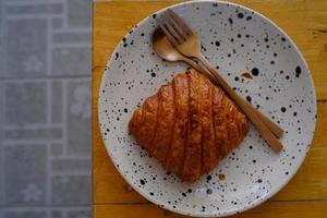 Fresh french croissant on white ceramic plate on wooden table photo