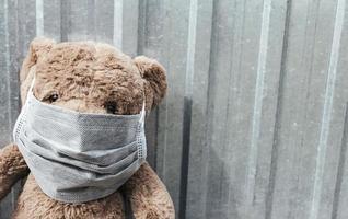 Cerca de un oso de peluche con máscara médica sentado cerca de la valla metálica. foto