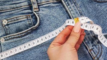 A female hand holds a measuring tape on a denim background photo