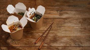 Noodles with pork and vegetables in take-out box on wooden table photo
