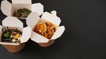 Noodles with pork and vegetables in take-out box on black table