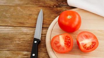 corte el tomate en una tabla de cortar de madera. cuchillo y tomates en madera foto