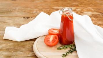 Jugo de tomate en botella de vidrio y tomates frescos sobre fondo de madera foto