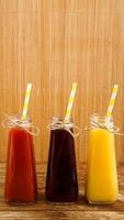 Three multicolored drinks in the bottles on a wooden bamboo background photo