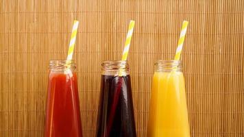 Tres bebidas multicolores en las botellas sobre un fondo de bambú de madera foto