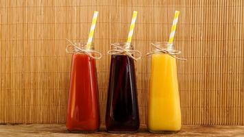 Three multicolored drinks in the bottles on a wooden bamboo background photo